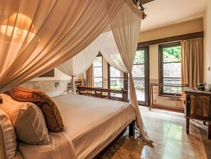 A bedroom with a four-poster bed, a wooden desk, and a view of the outdoors through large windows. - Villa 'Villa Semadhi' mit Infinity-Pool by Interhome (Buleleng)
