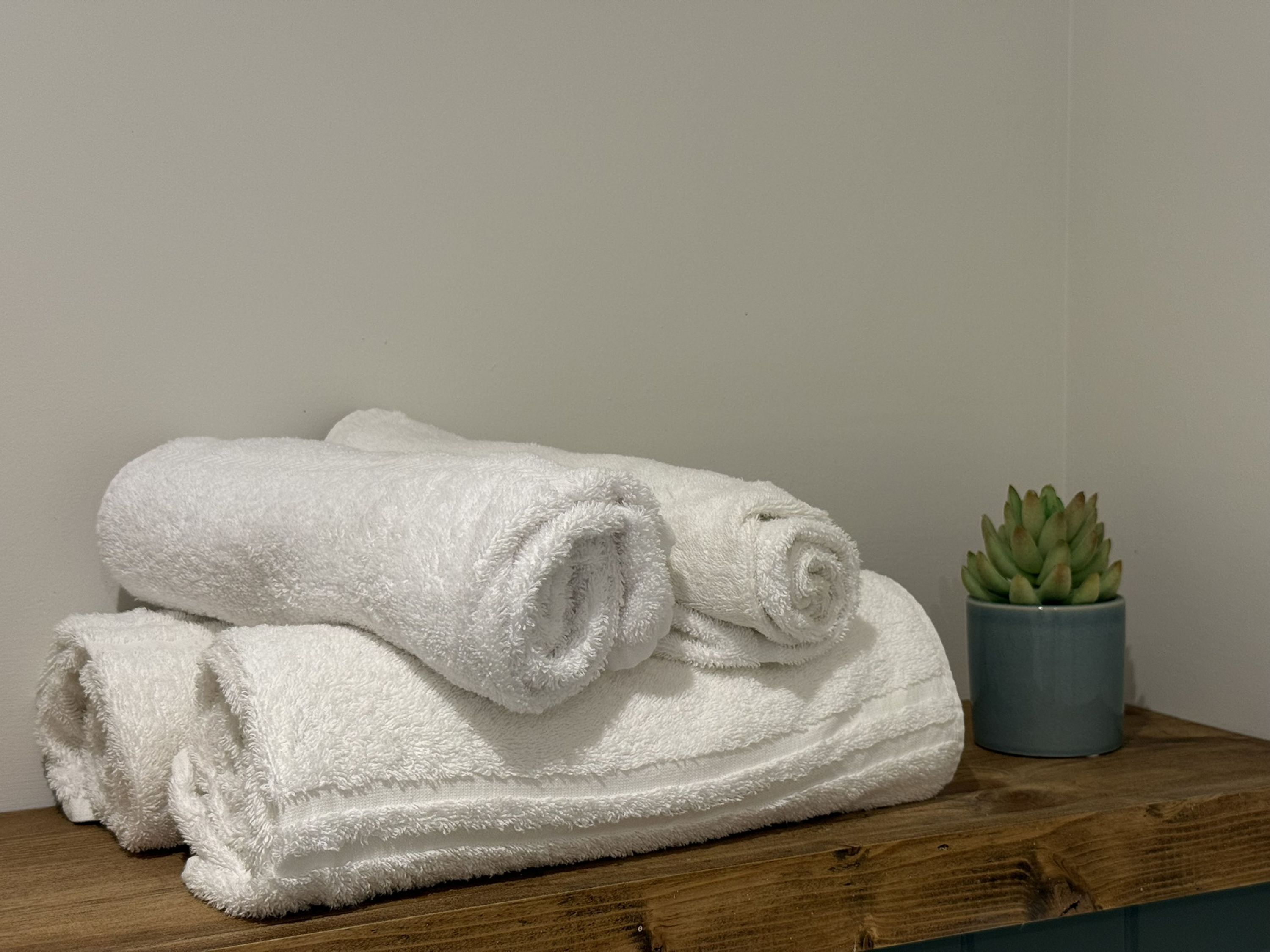 Een stapel witte handdoeken op een houten oppervlak, met een potplant ernaast.