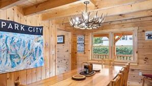 Un interior de madera con una mesa de comedor, sillas, un candelabro y un mapa grande en la pared.
