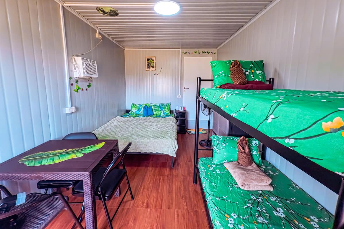 A compact room with a bunk bed, a desk with a chair, a fan, and a small shelf.