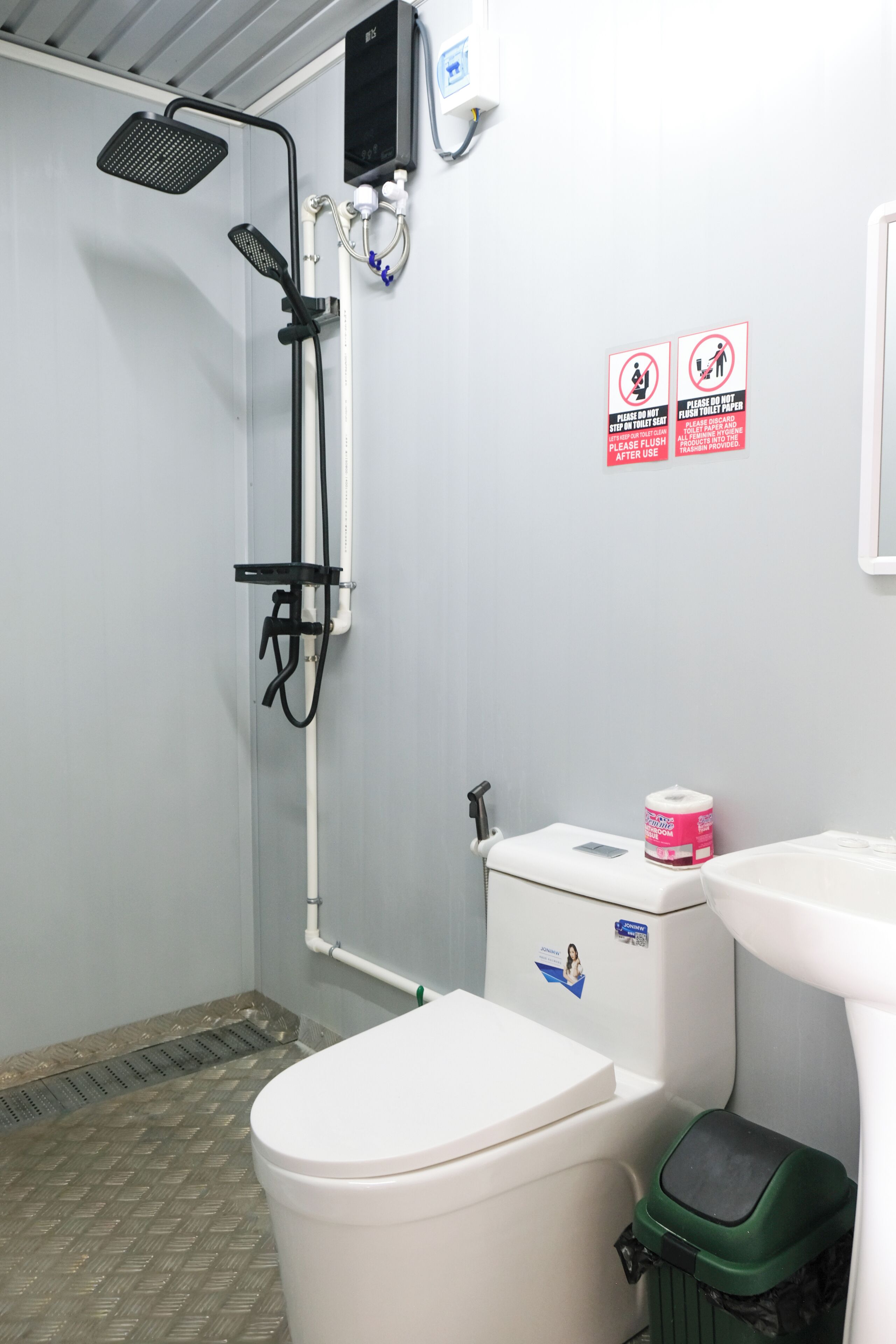 Un baño con ducha, inodoro y bidé. Hay letreros en la pared y un cubo de basura.