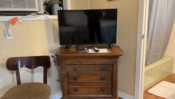 Une commode en bois, un téléviseur à écran plat, une chaise et un petit tapis.