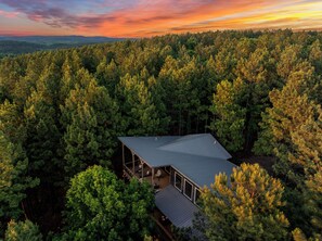 Ein Haus, umgeben von dichtem Wald, mit einer großen Terrasse und einem Metalldach.