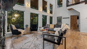 A spacious living area with large windows, a fireplace, and a cozy seating arrangement. - Dual Deck Hangouts/Game Loft/Hot Tub/Hochatown! (BROKEN BOW)