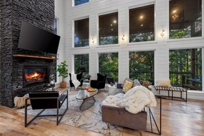 Ein geräumiges Wohnzimmer mit Kamin aus Stein, großen Fenstern und einer gemütlichen Sitzecke.