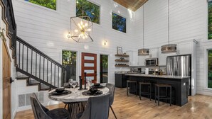 A spacious kitchen with a central island, a dining area with a round table and chairs, and a staircase leading to an upper level. - Dual Deck Hangouts/Game Loft/Hot Tub/Hochatown! (BROKEN BOW)
