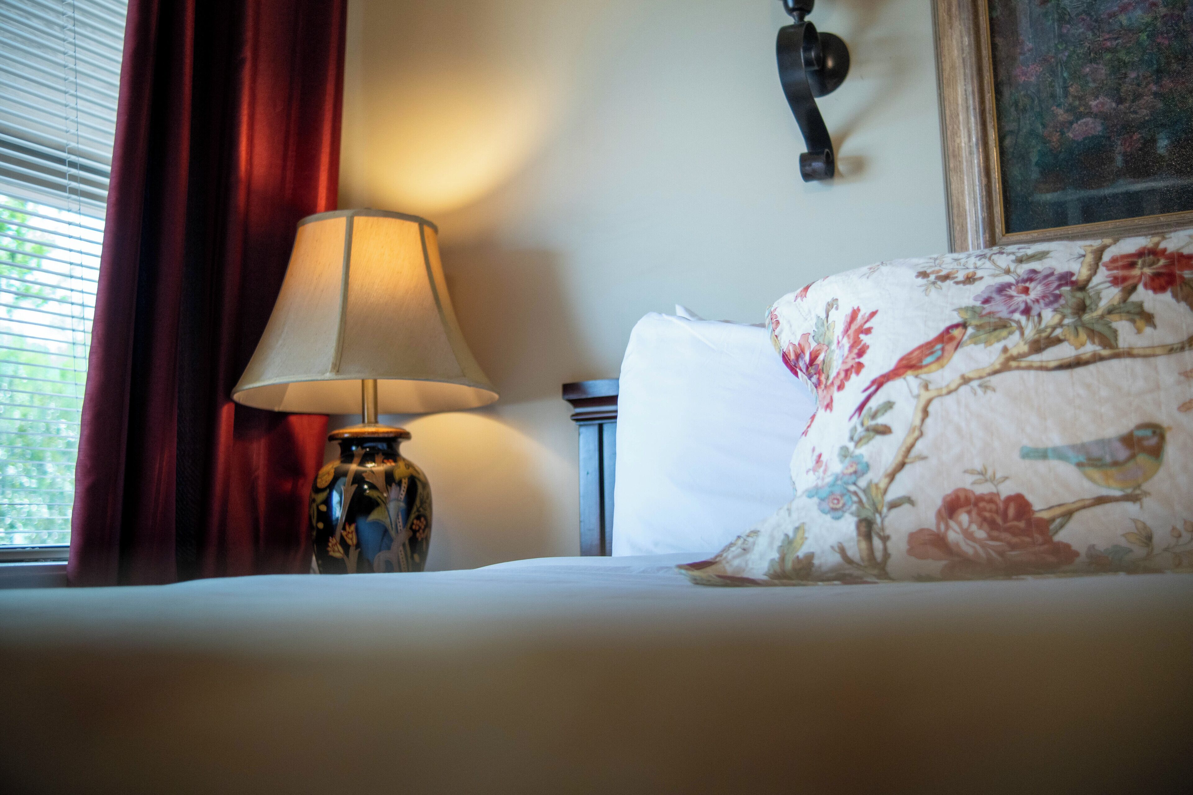 A bed with floral bedding, a lamp, and a painting on the wall.