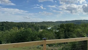 Una terraza de madera con barandilla metálica que da vista a un valle boscoso con un río.