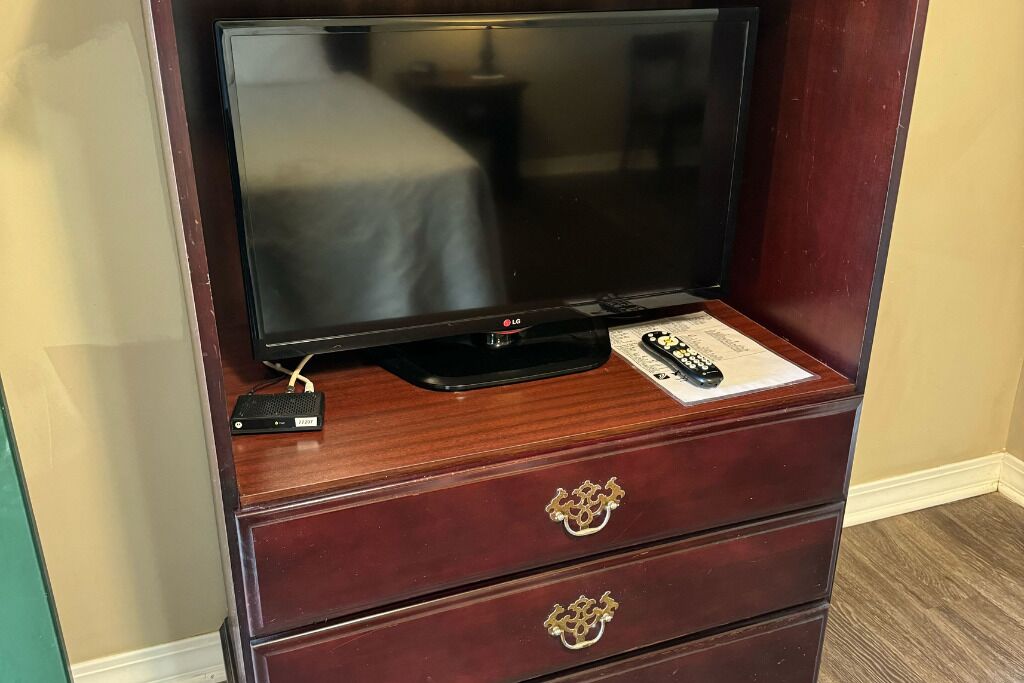 A television on a wooden cabinet with a remote control and a keychain on top.