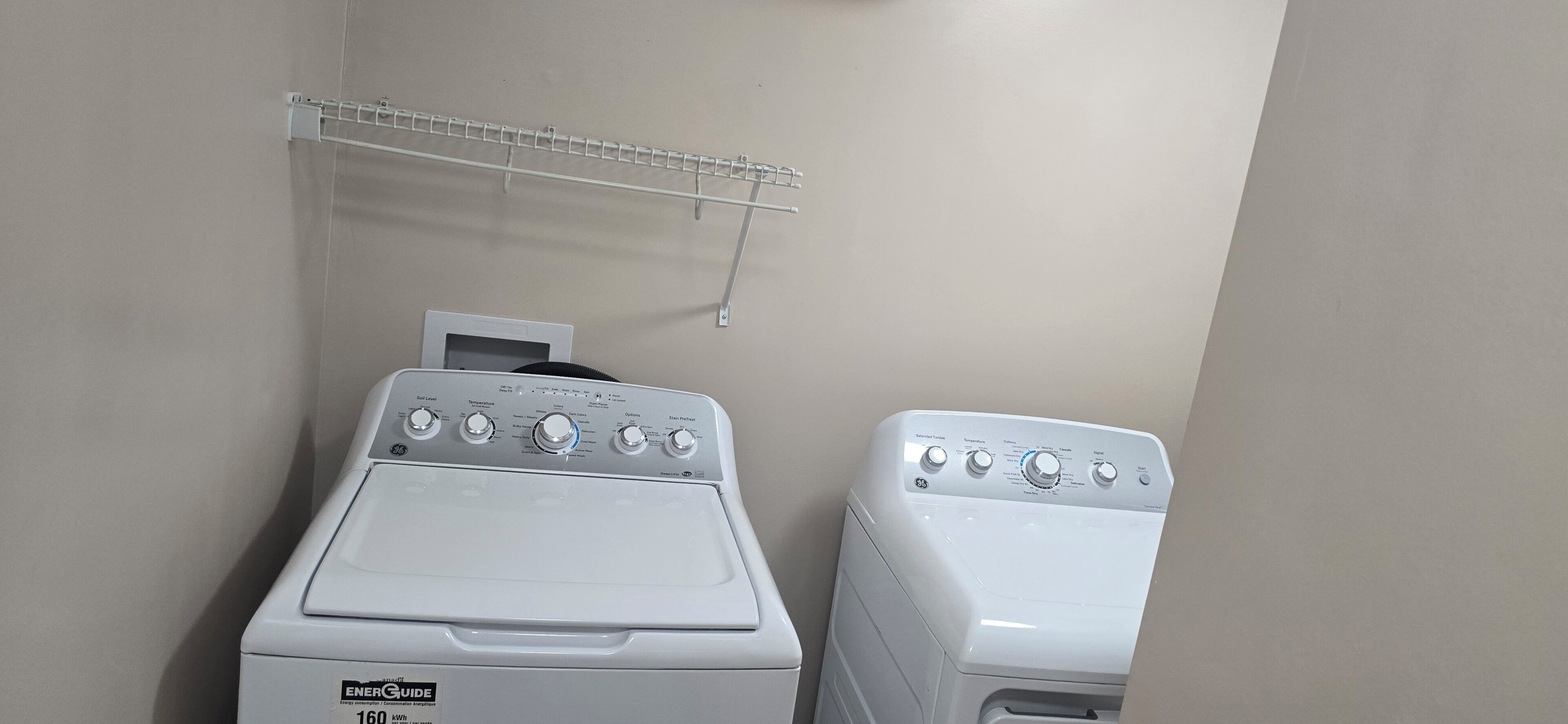 Two front-loading washing machines in a laundry room with a white wall and a metal drying rack.