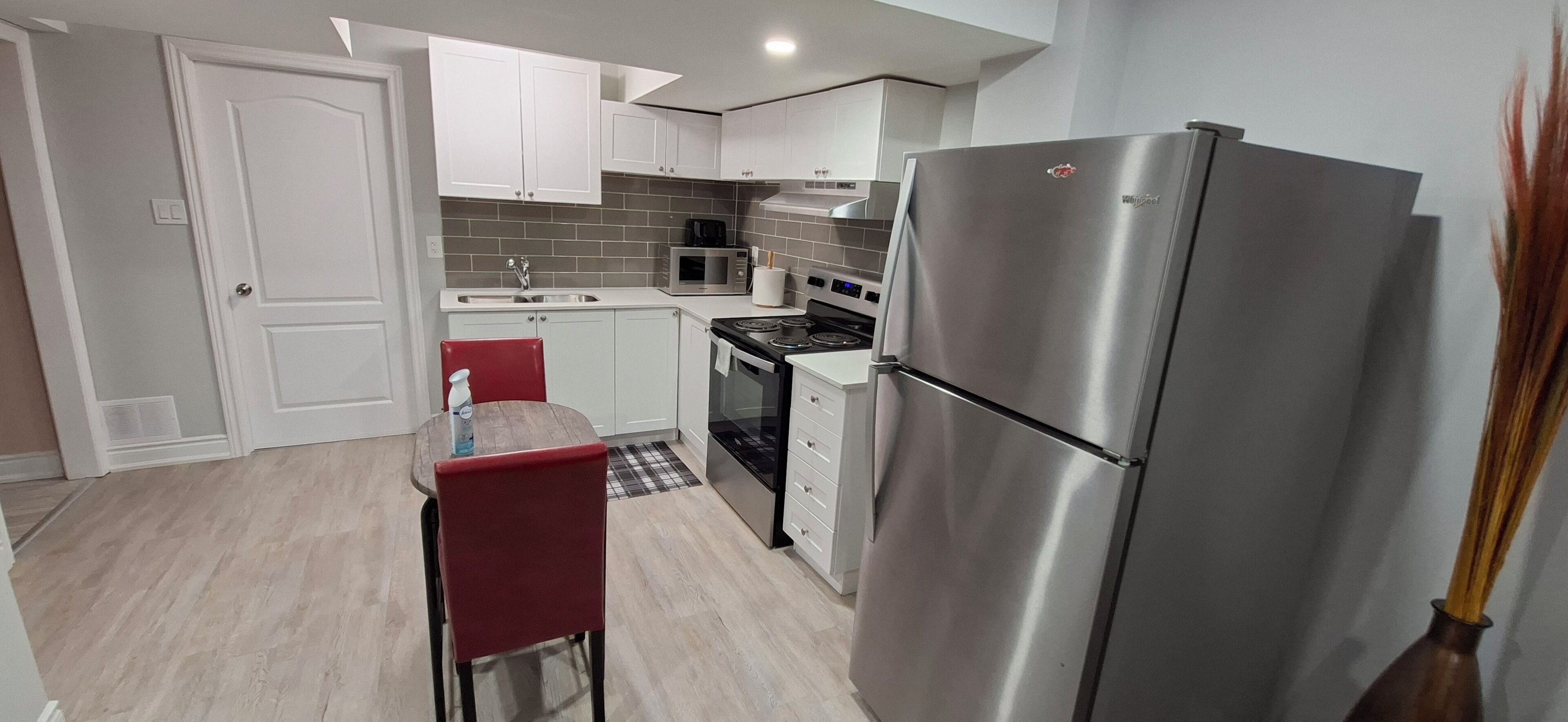 Una cocina compacta con armarios blancos, un refrigerador de acero inoxidable, un microondas y una estufa.