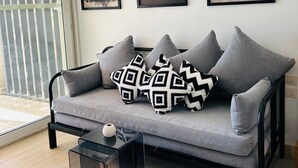 A modern living room with a grey sofa, black and white patterned pillows, a glass coffee table, and three framed artworks on the wall. - Hacienda Bay Lagoon Cabin | Beachfront Escape (Sidi abdelrahman , al Alamein)