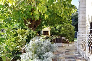 Une terrasse en pierre avec un banc en bois, une petite structure en bois et une clôture en métal blanche.