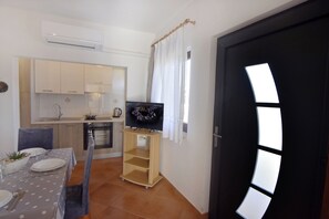 Une cuisine compacte avec un coin repas, un téléviseur posé sur un meuble et une porte dotée d’un design de fenêtre original.