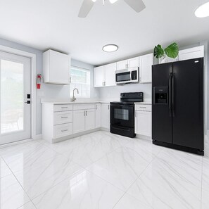 A modern kitchen with white cabinets, a black refrigerator, a microwave, and an oven.