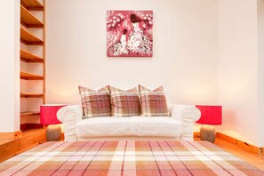 A white sofa with plaid cushions, a red and white plaid rug, and a painting of a woman in a white dress. - Two Miles From Town (Inverness)