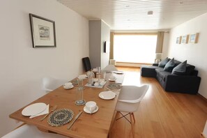 A dining area with a wooden table set for four, a sofa, and a large window. - Two Miles From Town (Inverness)