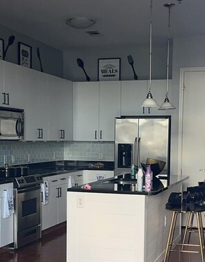 A modern kitchen with white cabinetry, a stainless steel refrigerator, a stove, and a bar area with stools.