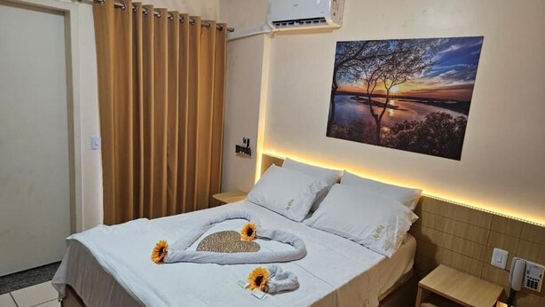Ein Hotelzimmer mit Bett, einem Sonnenuntergangsbild, einer Klimaanlage und einem Nachttisch mit Lampe.