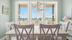 Ein Essbereich mit Tisch und Stühlen, einer Hängeleuchte und Blick durch große Fenster.