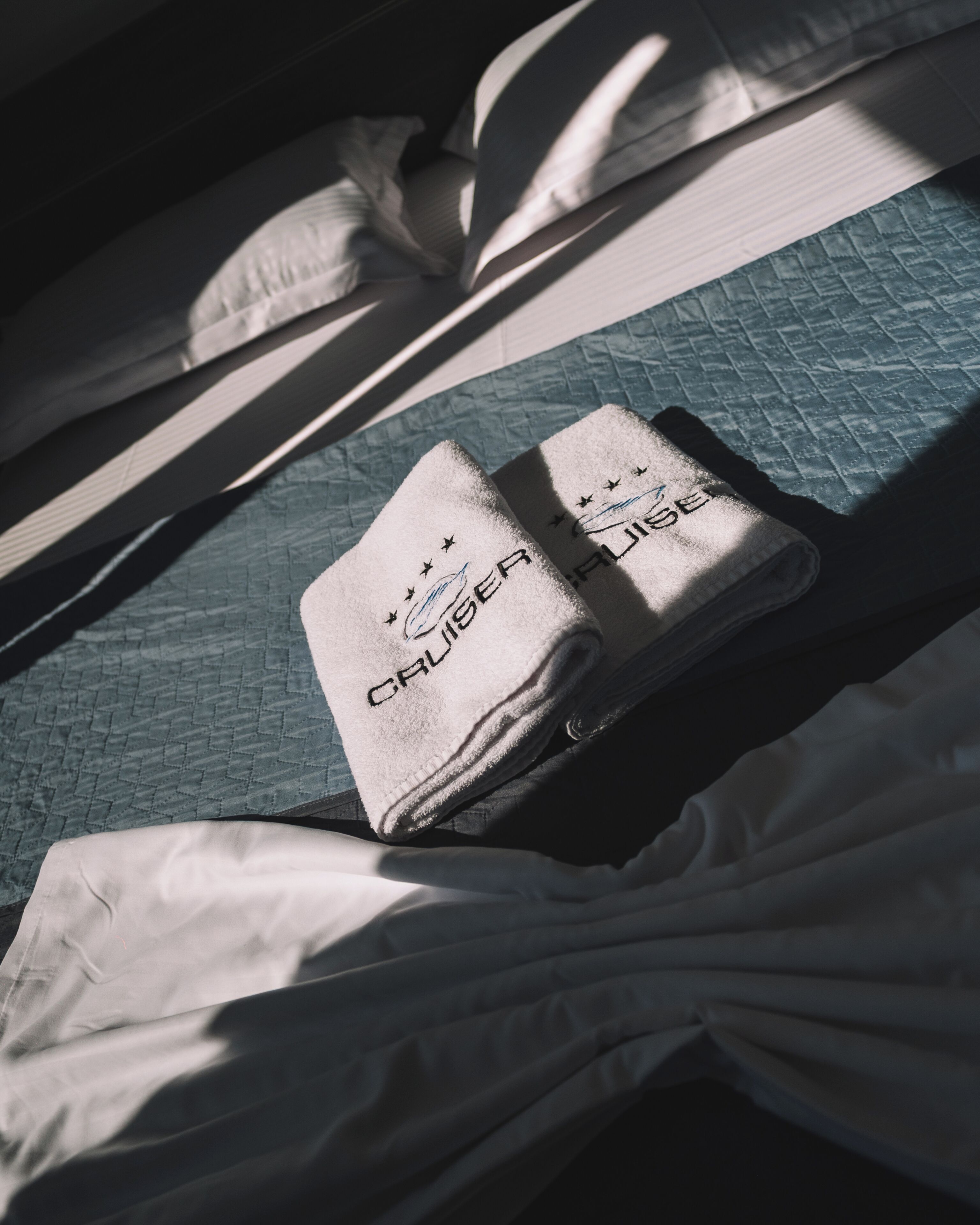 A bed with neatly folded towels and a quilted blue bedspread.