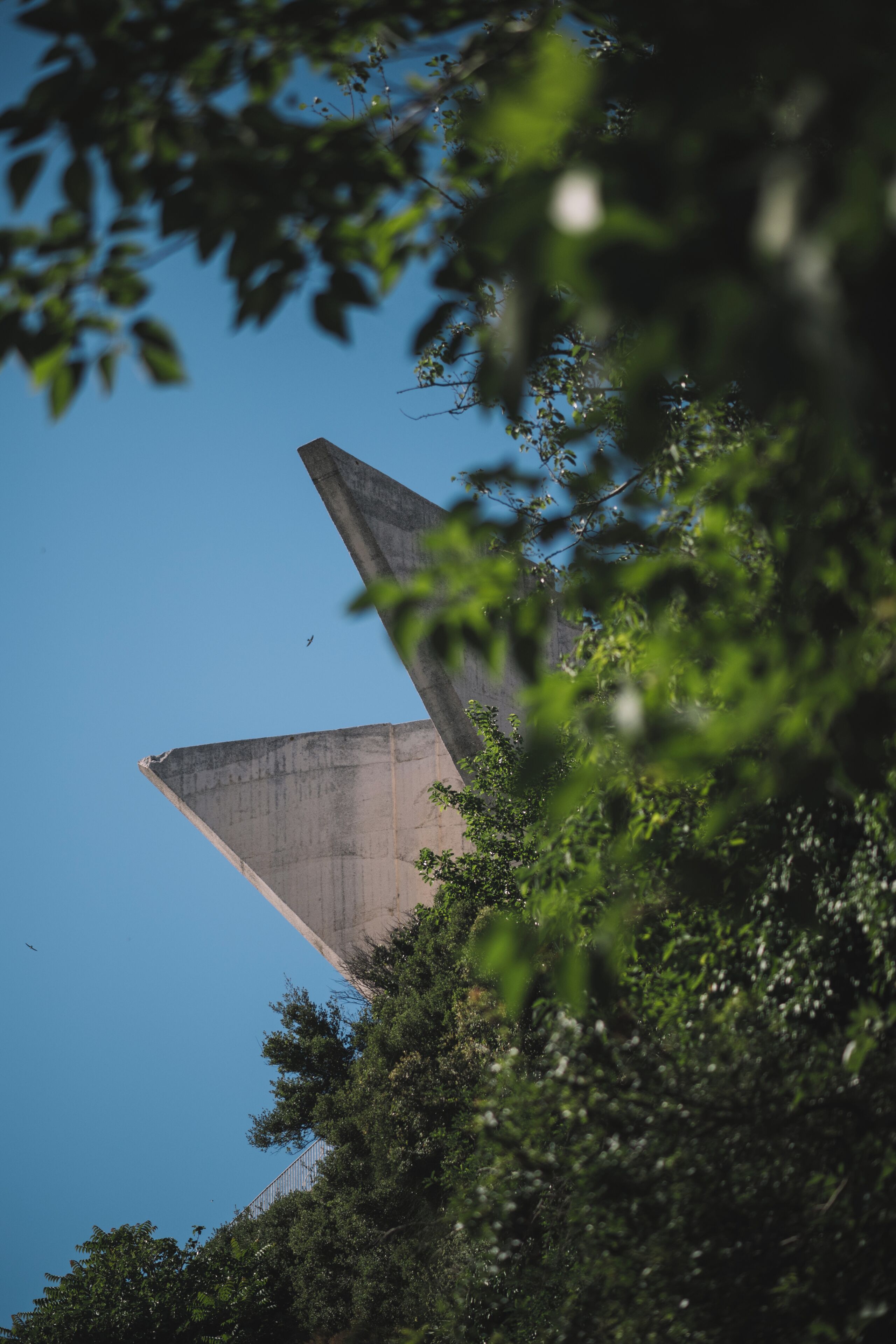A large concrete structure with a pointed tip, surrounded by dense foliage.