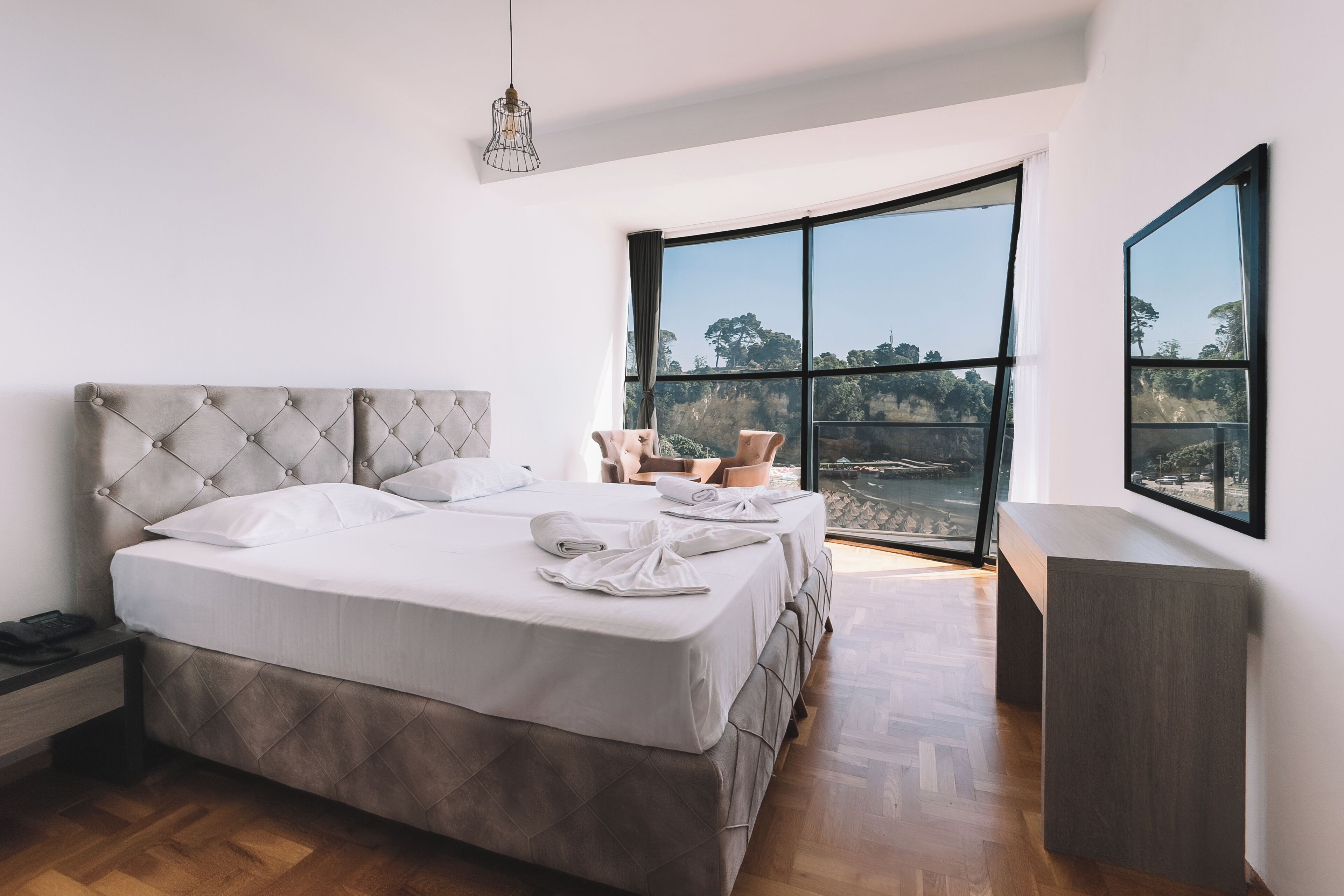 A bedroom with a large bed, two chairs, a nightstand, and a view of the outdoors.