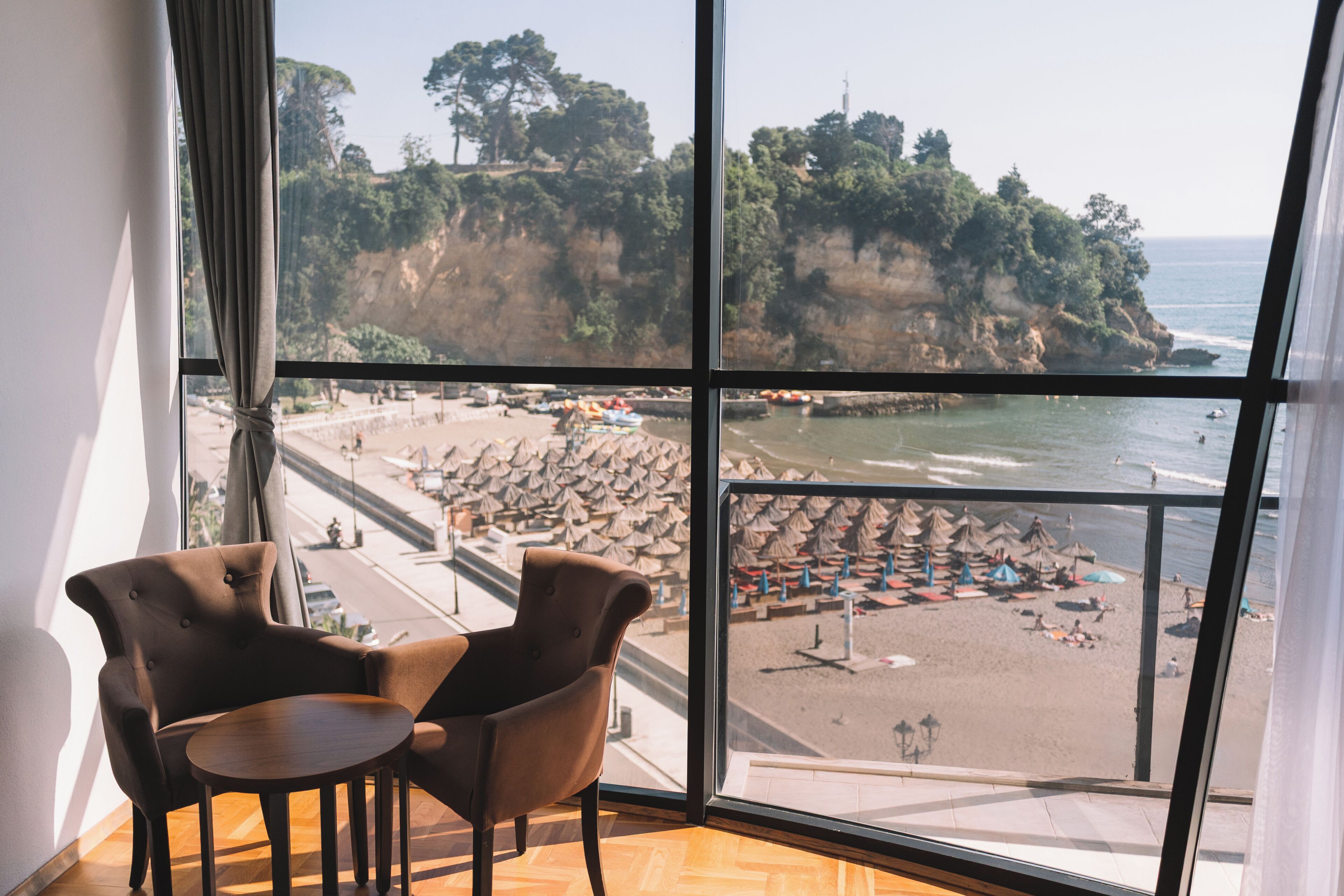 A room with a large window overlooking a beach, a chair, and a small table.
