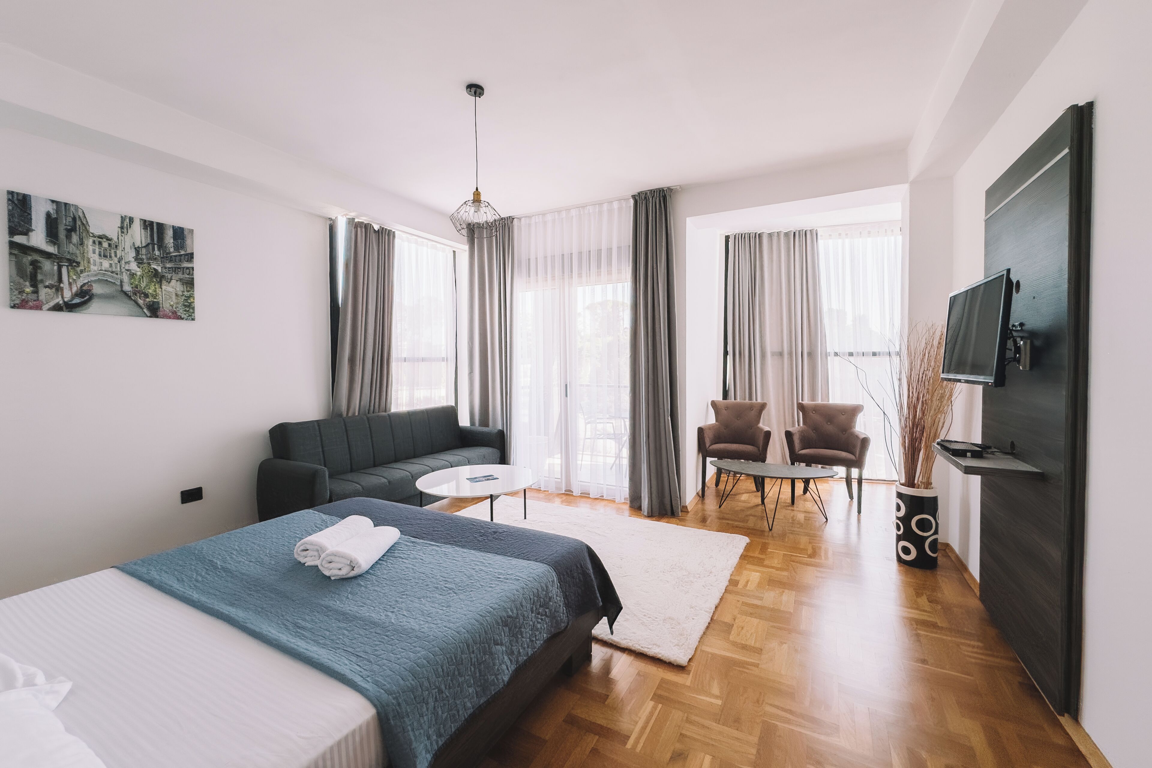 Une chambre d’hôtel moderne, équipée d’un lit, d’un canapé, d’une table à manger, de chaises, d’un téléviseur et d’un tableau au mur.