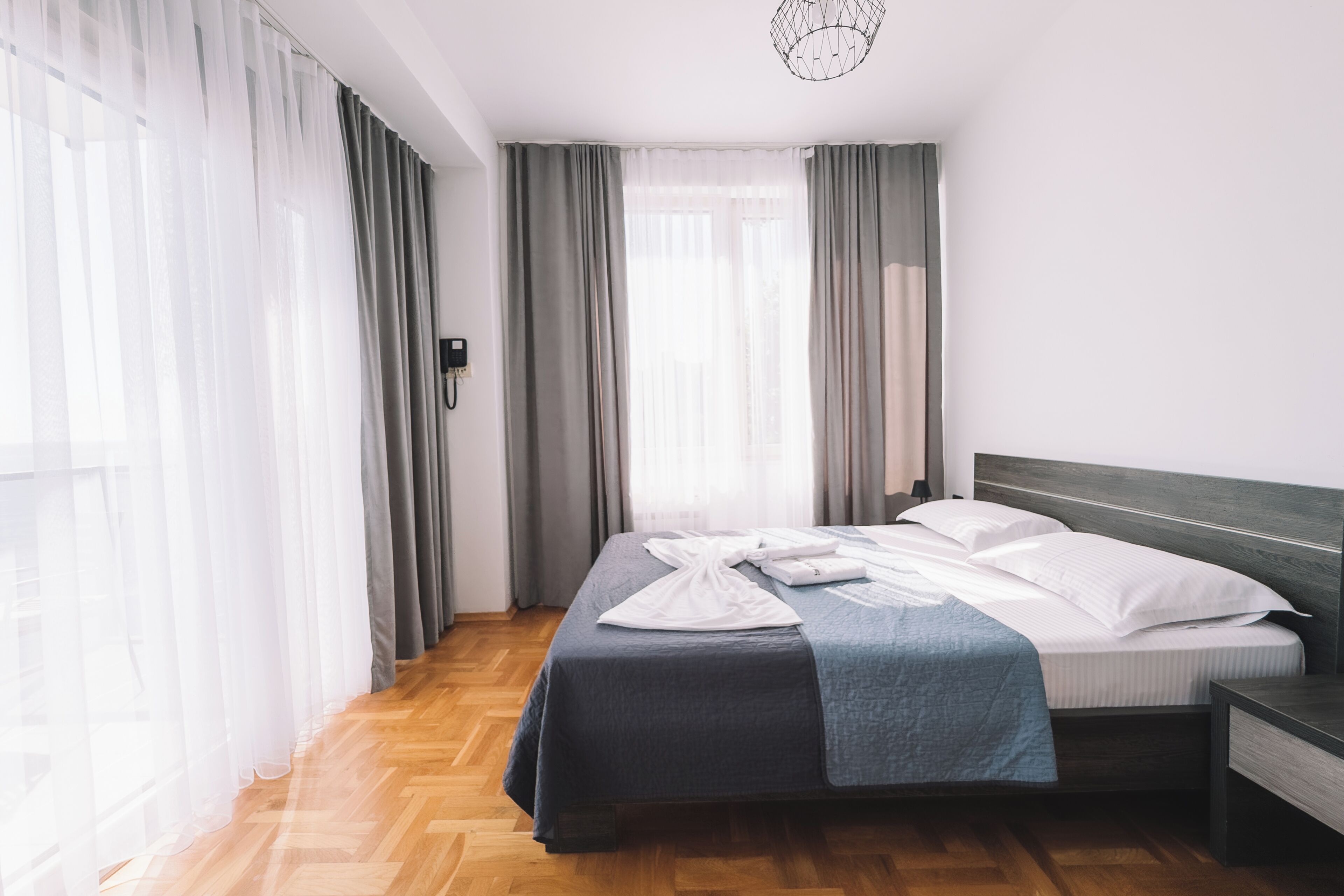 Een hotelkamer met een bed, nachtkastje en een raam met gordijnen.
