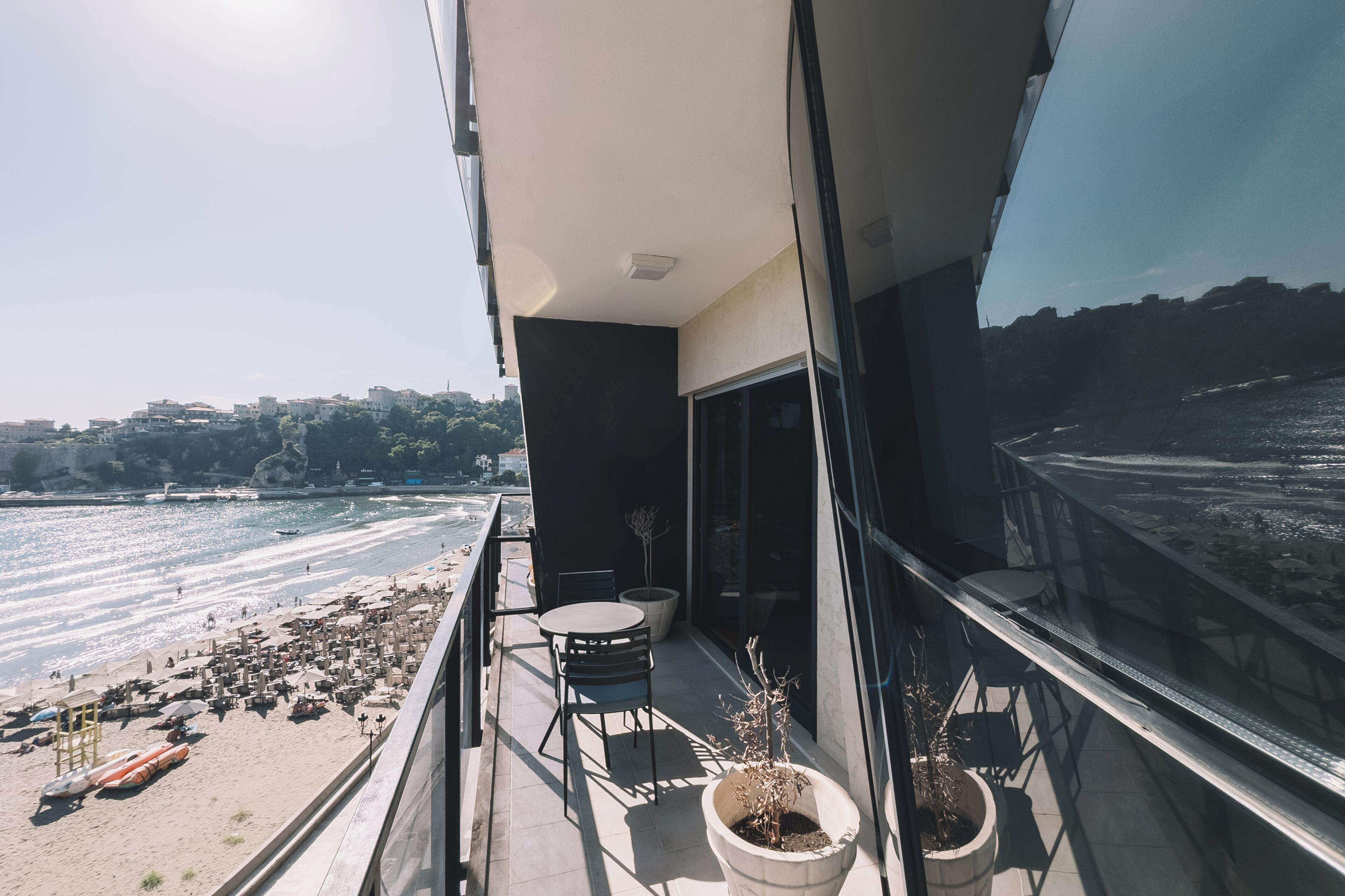 A balcony with a view of the beach, a table, chairs, and potted plants.