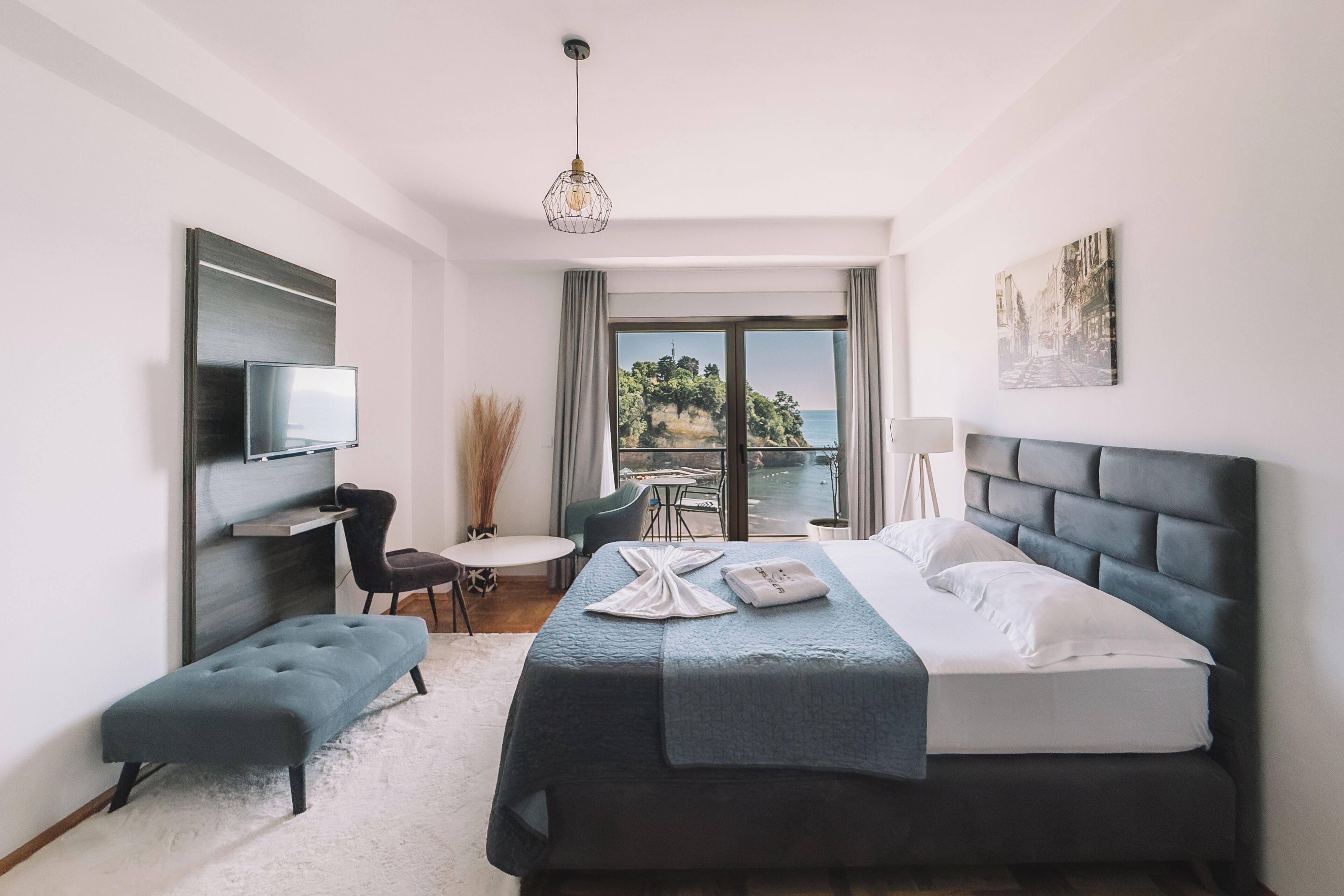 A modern hotel room with a bed, seating area, TV, and a view of the outdoors.