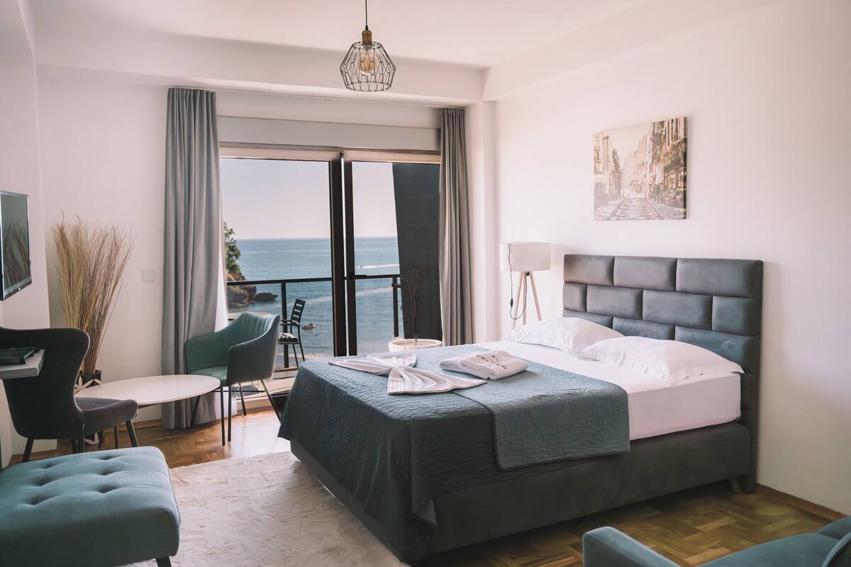 Un dormitorio con cama, escritorio, silla, sofá y vista al océano.