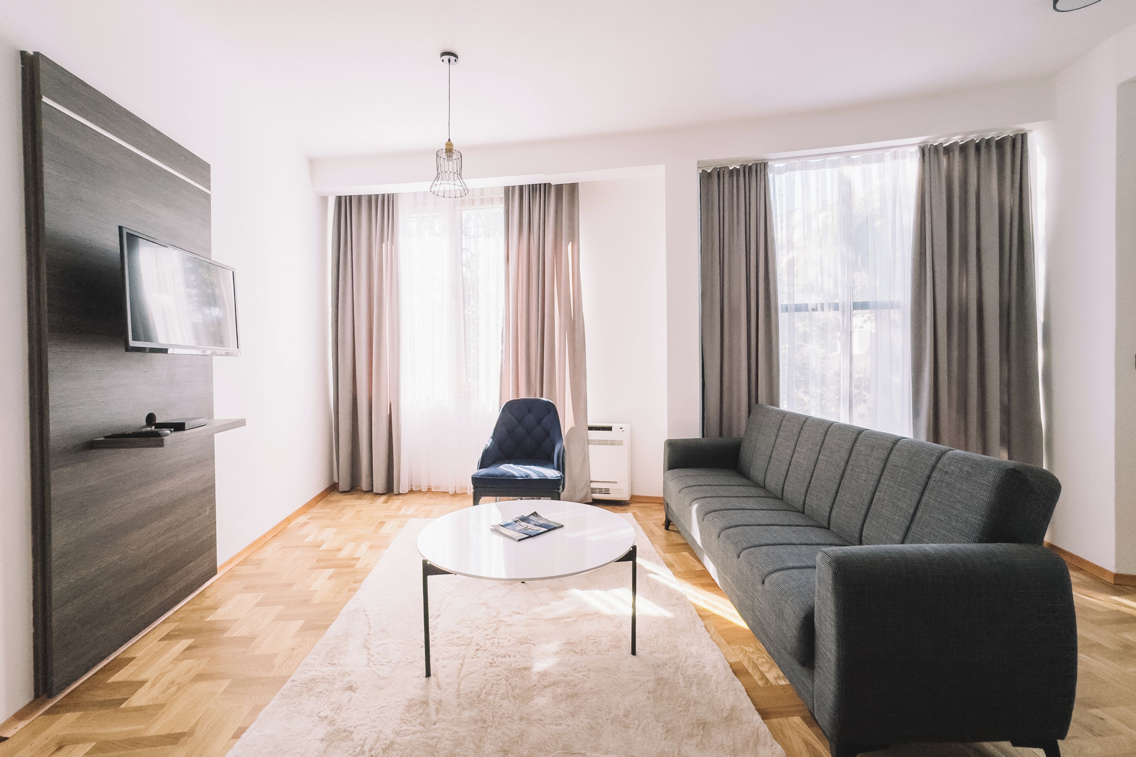 A modern living room with a sofa, a flat-screen TV, a chair, and a large window with curtains.