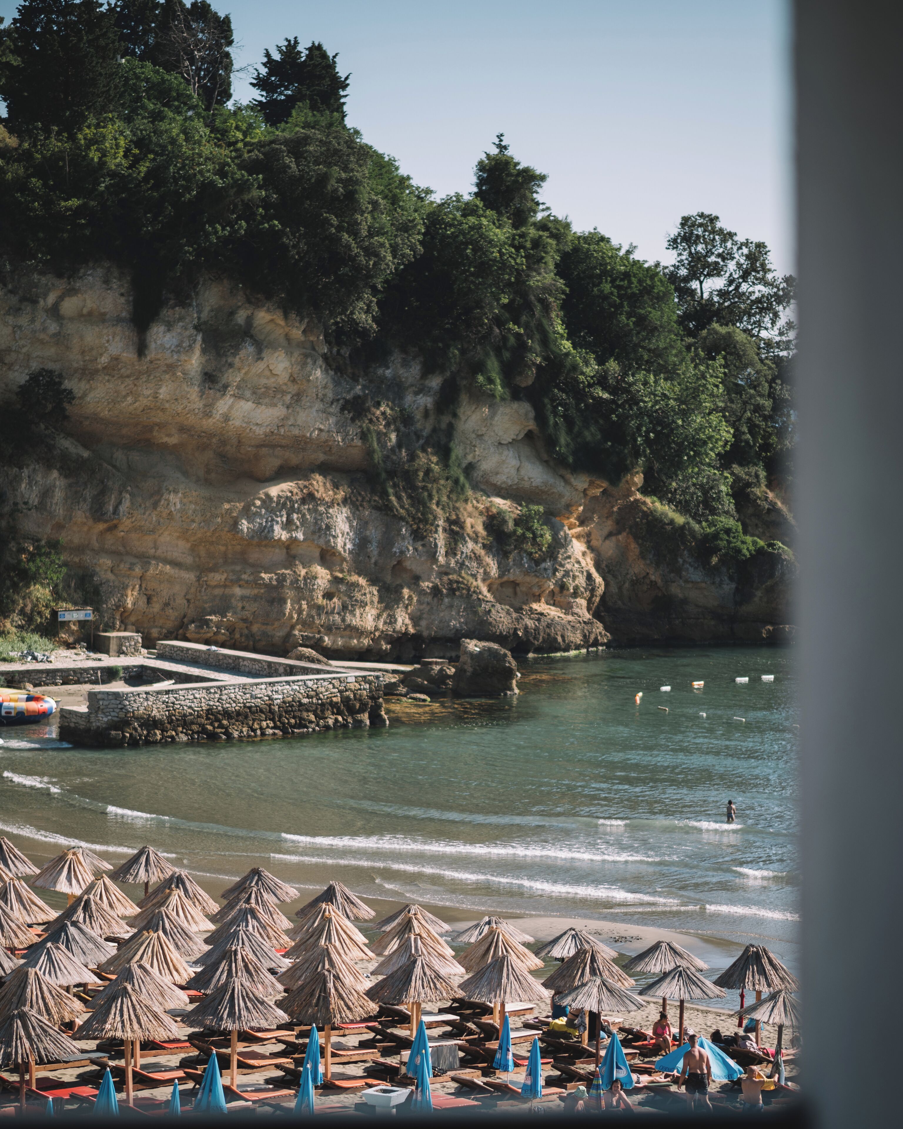 A beach with umbrellas, a rocky cliff, and a calm sea.