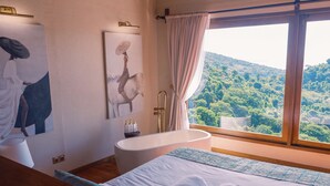 A bedroom with a large window, a bathtub, and artwork on the wall. - Organic Luxury Villa with Infinity Pool & Ocean Views (Karangasem)