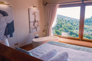 A bedroom with a large window, a bathtub, and artwork on the wall. - Organic Luxury Villa with Infinity Pool & Ocean Views (Karangasem)