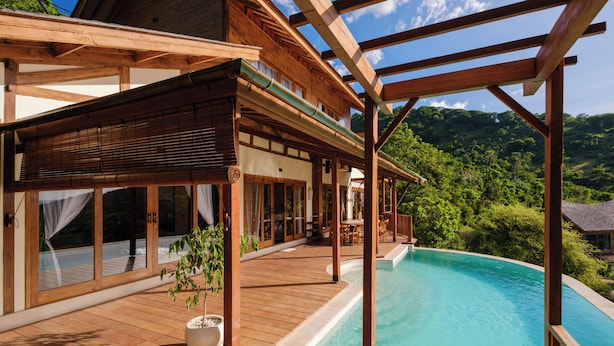 A wooden deck with a swimming pool, large windows, and a view of a mountainous landscape. - Organic Luxury Villa with Infinity Pool & Ocean Views (Karangasem)