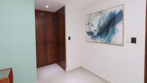 Un pasillo con una puerta de madera, una pared blanca con un cuadro abstracto azul y un suelo de baldosas.
