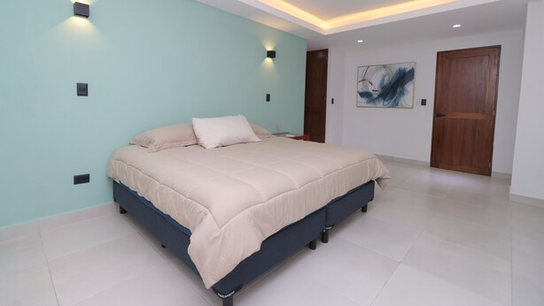 Un dormitorio con cama, ventilador de techo, luces empotradas y una puerta.