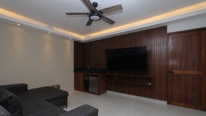 Una sala de estar moderna con un televisor de pantalla plana, sofás oscuros, un ventilador de techo y paneles de madera.