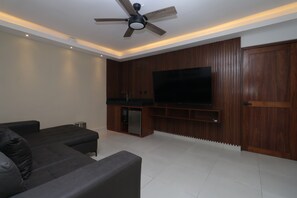 Ein modernes Wohnzimmer mit Flachbildfernseher, dunklen Sofas, Deckenventilator und Holzvertäfelung.