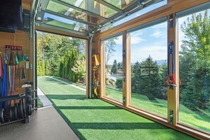 Ein moderner Fitnessraum mit großen Fenstern, einer digitalen Uhr und Trainingsgeräten.