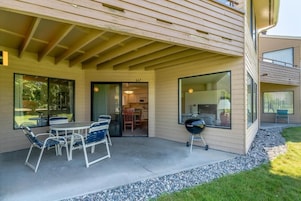 Un patio techado con una mesa y sillas de comedor, una parrilla y una cocina visible a través de puertas de vidrio.