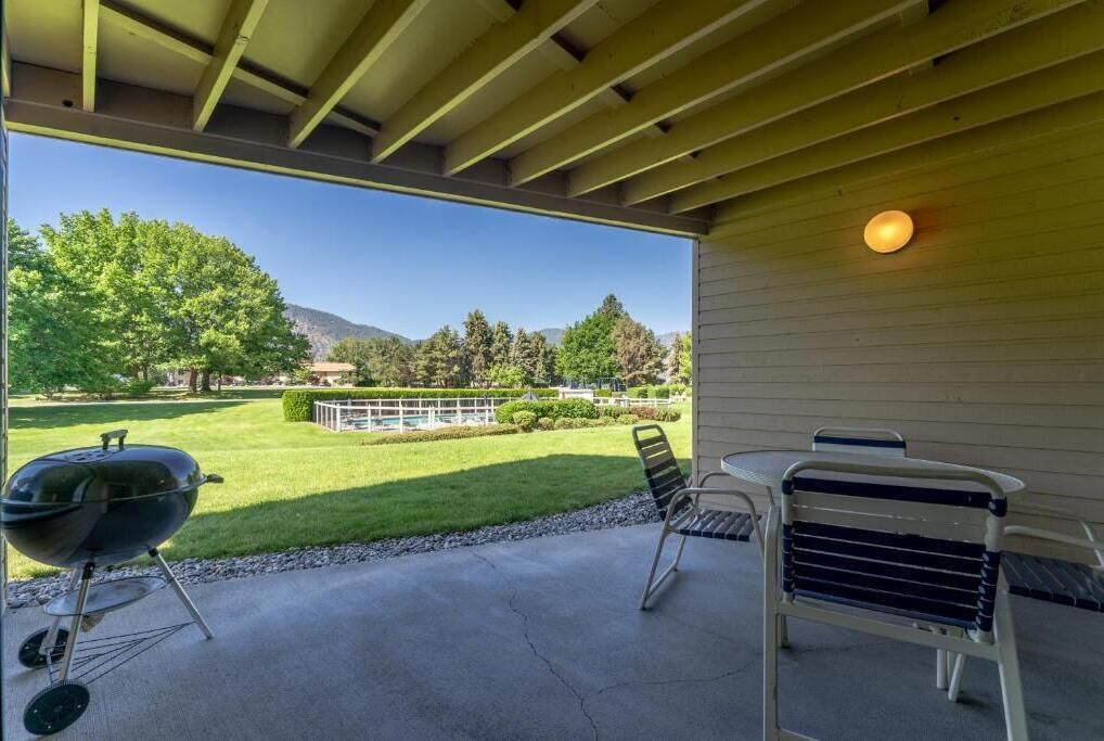 Un patio al aire libre con una parrilla, sillas y vistas a un paisaje verde.