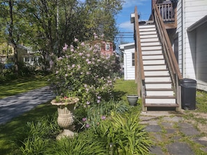 A residential garden with a stone pathway, a bird bath, and a staircase leading to a house.