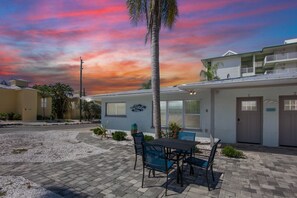 A building with a patio area, a table with chairs, and a palm tree. - Beautiful 2 Bedroom Duplex Steps Away from the Beach (Sarasota)