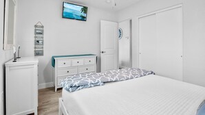 Quarto com cama, penteadeira, cômoda, televisão e porta.