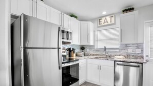 Uma cozinha moderna com eletrodomésticos de aço inoxidável, armários brancos e bancada com painel decorativo.