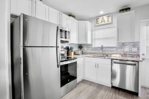 Una cucina moderna con elettrodomestici in acciaio inossidabile, mobili bianchi e un piano di lavoro con rivestimento.